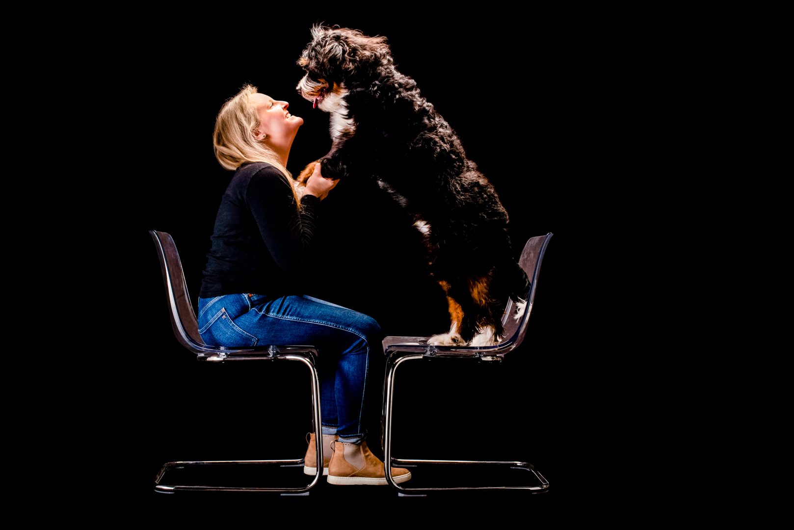 Chicago Dog Photographer, Cusic Photo, captures families and dogs together in her Chicago studio. Image of woman with blond hair, jeans and a black shirt holding hands / paws with fluffy black and white dog.