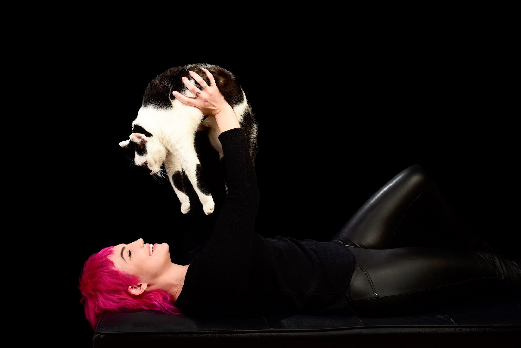 Woman with pink hair holding black and white tabby cat