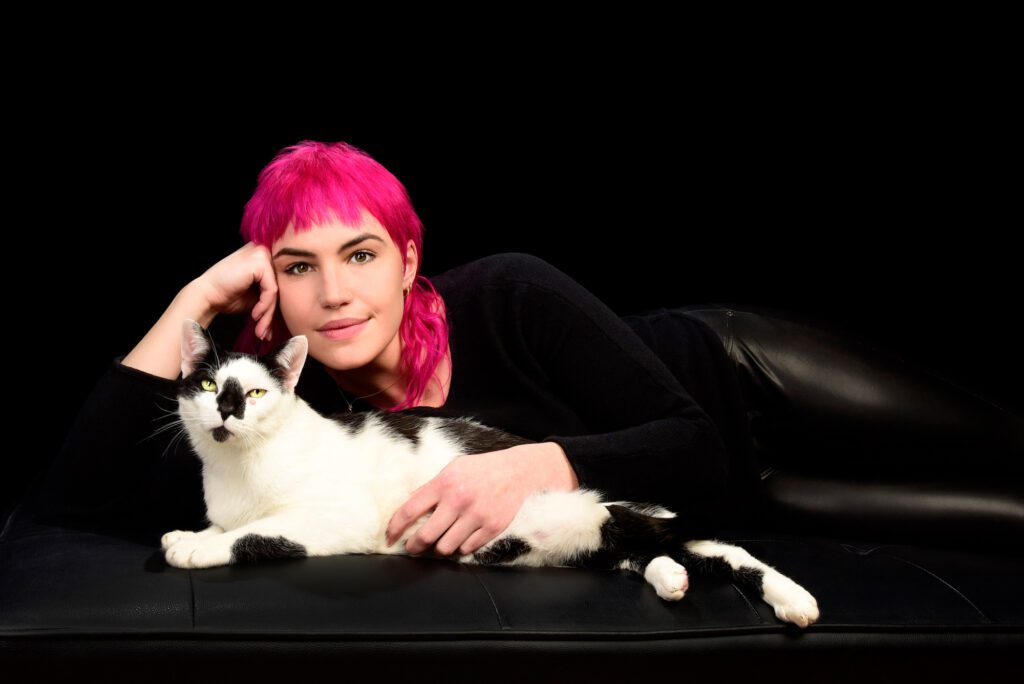 woman with pink hair laying down with tuxedo cat